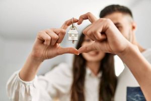 Young couple doing heart symbol with fingers and holding key of new home.
